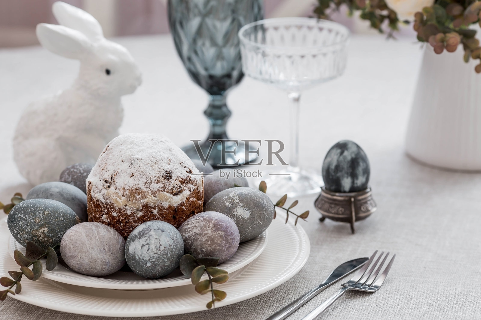 弹簧桌设置。一个盘子，一个有兔子的棉餐巾，一个蛋糕和复活节彩蛋。银器，复活节兔子，亚麻桌布上的花瓶。一个明亮的复活节假期的概念。照片摄影图片