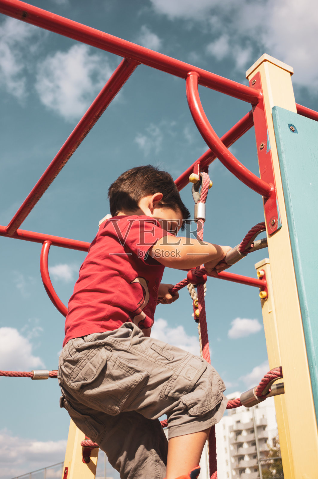 一个穿着红色t恤的白人男孩在户外操场上爬楼梯的特写照片摄影图片