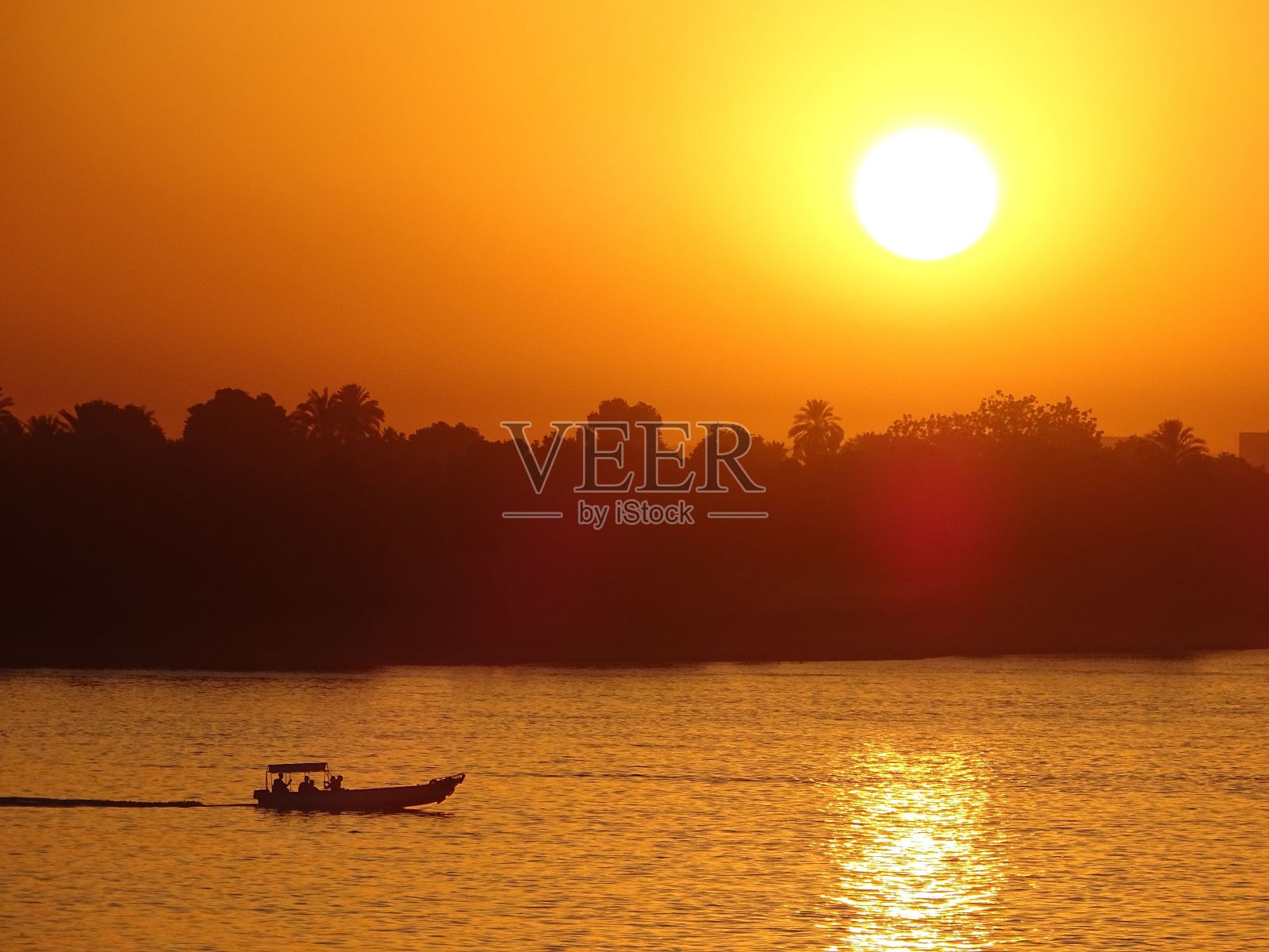 小船在平静的海岸上巡航，映衬着森林的剪影和明亮的日落照片摄影图片