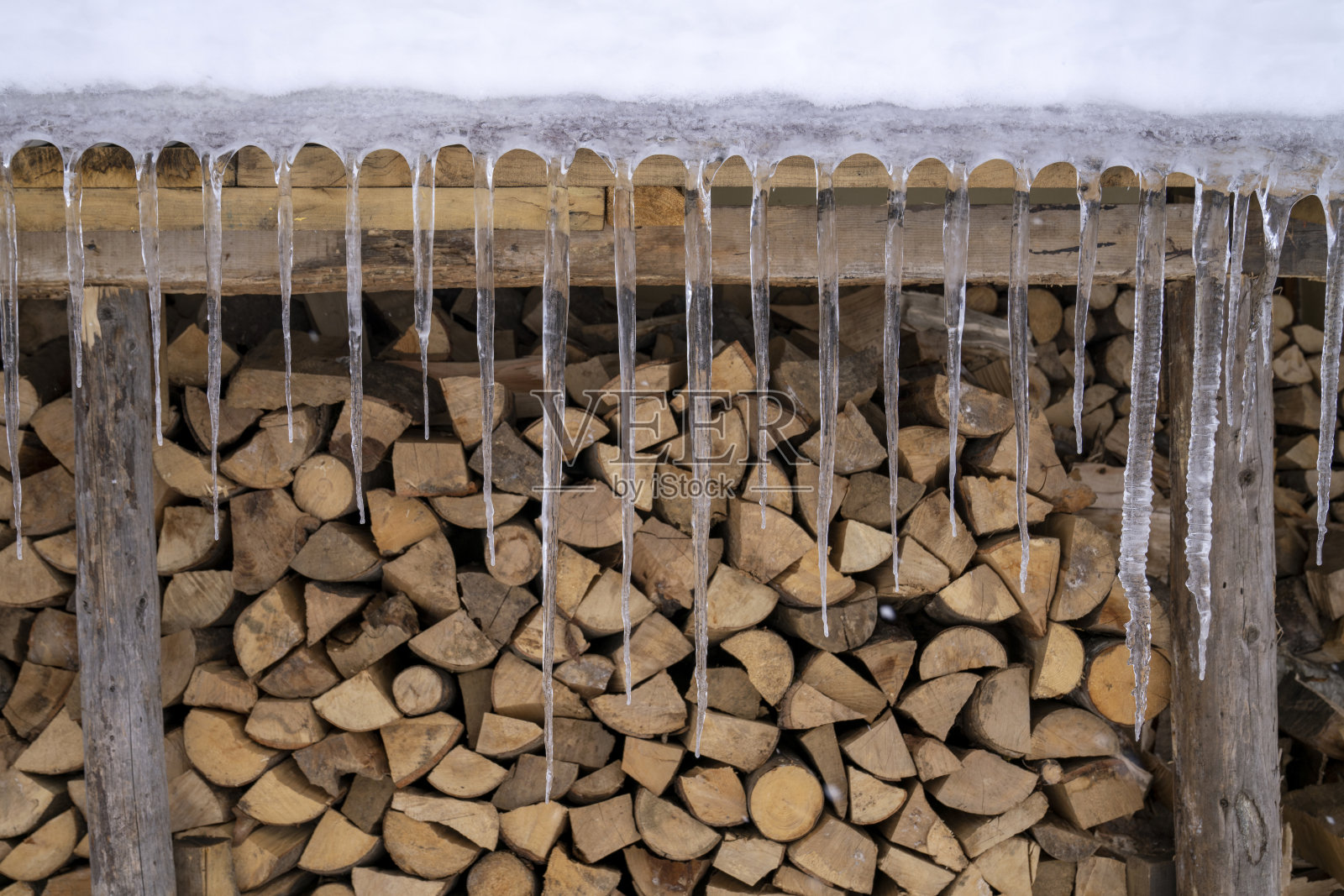 山上小屋的雪顶上挂着冰柱，还有成堆的木头照片摄影图片