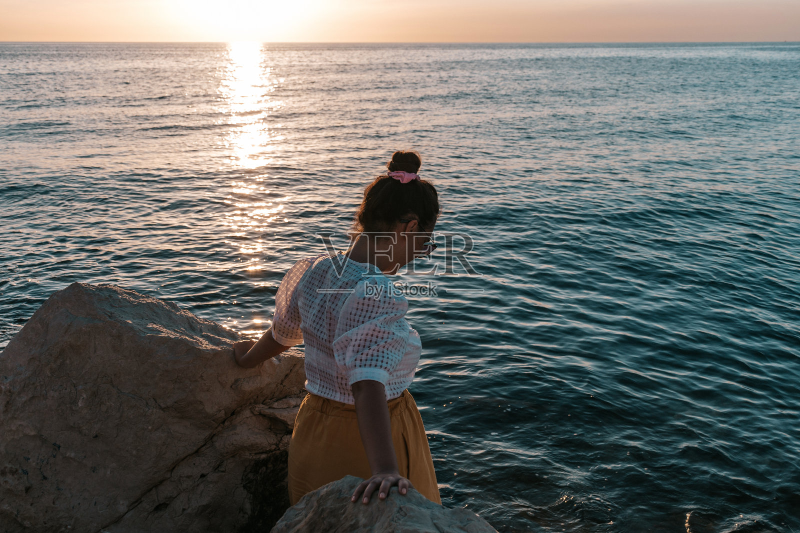 一位白人女性站在海边的两块大石头中间照片摄影图片