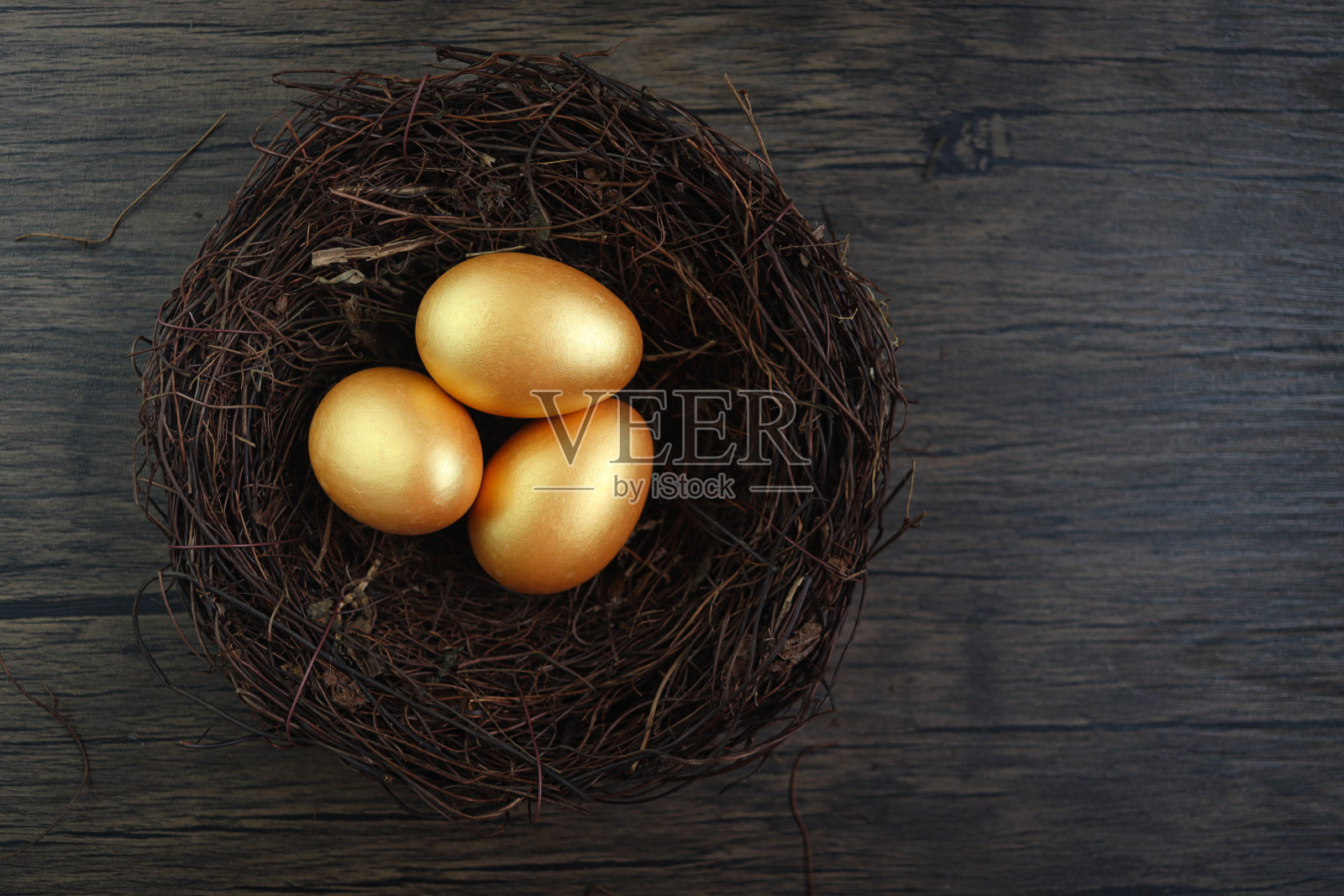 鸟窝里美丽的金色复活节彩蛋的俯视图，在质朴的棕色木质表面背景下，装饰和庆祝复活节和春天的开始。照片摄影图片