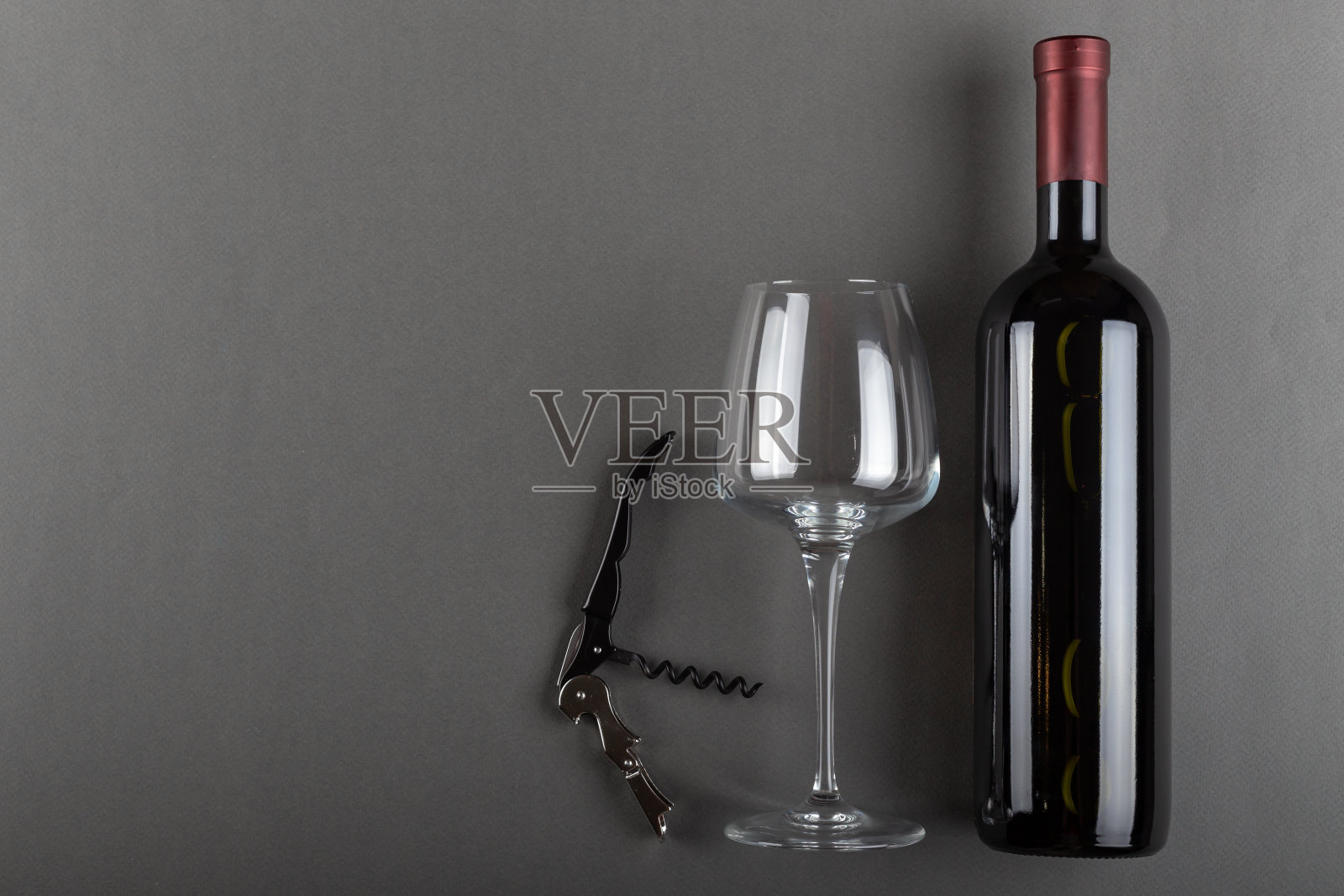 灰色背景上的红色酒瓶，开塞钻和空酒杯。酒精饮料。酿酒的概念。照片摄影图片
