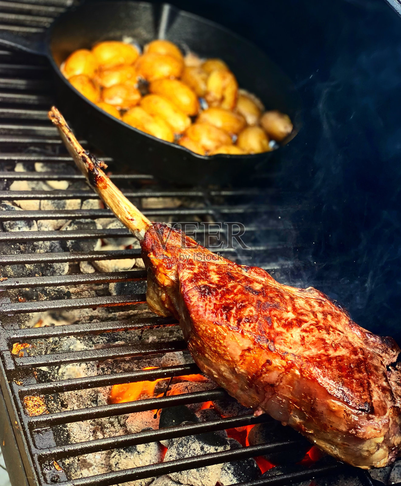 垂直镜头:烤肉架上烤着一片肉，旁边放着土豆照片摄影图片