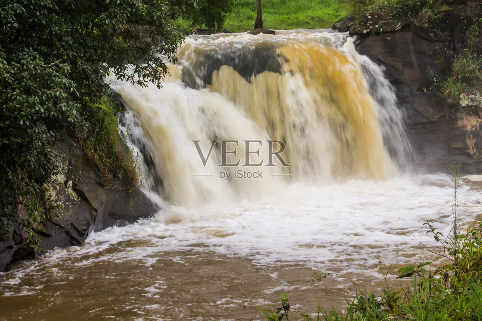从岩石上流出的浑浊的泡沫水，就像大雨后的瀑布照片摄影图片