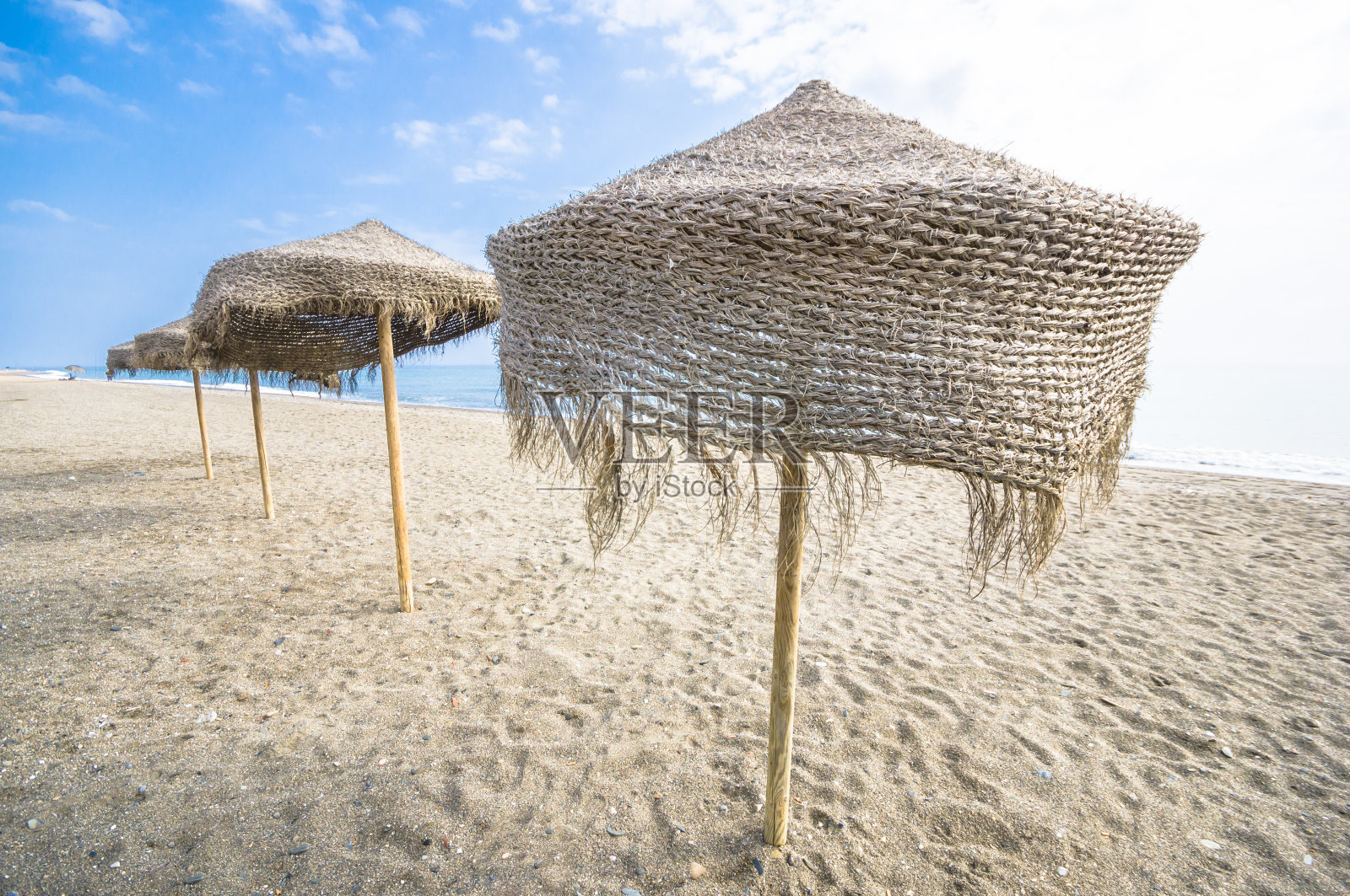 西班牙太阳海岸美丽的沙滩，一排排的稻草沙滩伞照片摄影图片