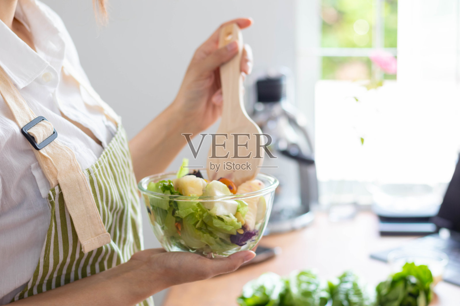 一名年轻女子正在用她在家里厨房桌子上准备的蔬菜做沙拉，因为配料是精心挑选的，所以沙拉是干净和安全的。健康食物准备方法照片摄影图片