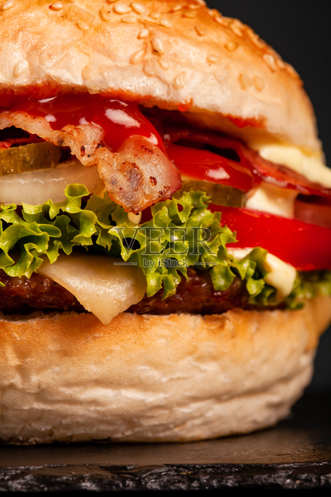 培根汉堡，洋葱，西红柿，黄瓜和生菜，深色背景。抽象的快餐照片。照片摄影图片