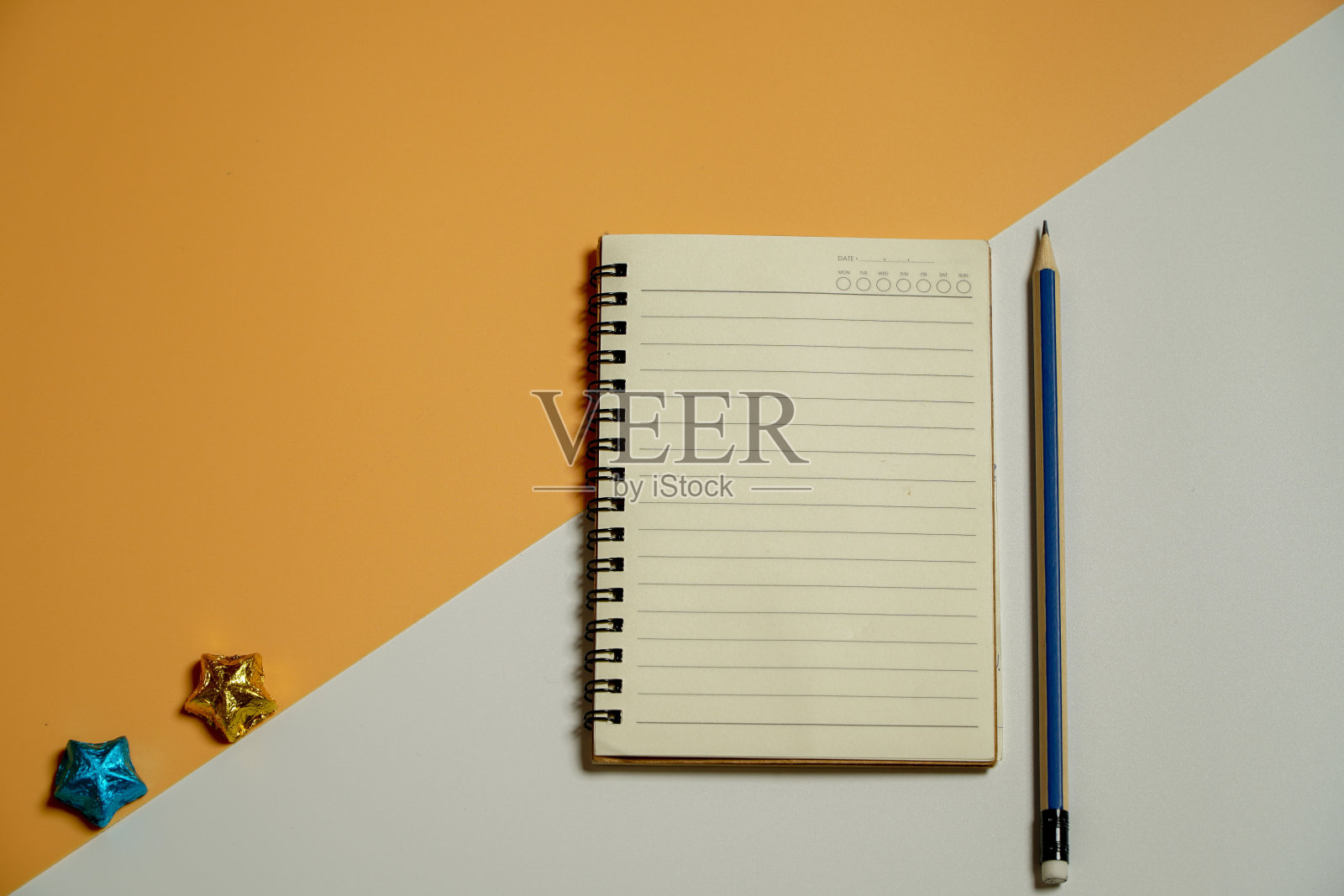 在头顶上接近平平视图清晰螺旋教科书的照片与铅笔画在一个橙色的一半分裂和白色的桌子。照片摄影图片