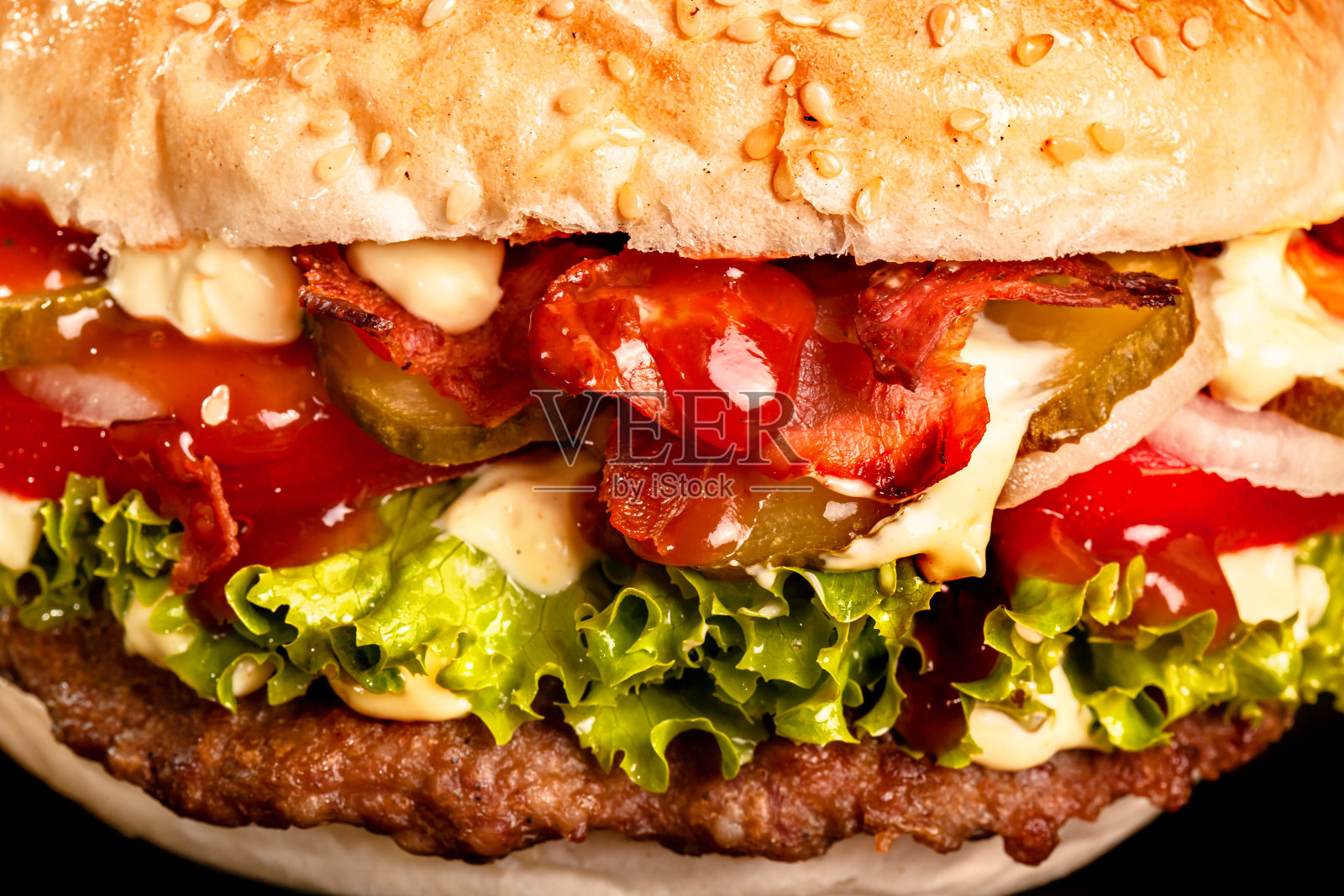 培根汉堡，洋葱，西红柿，黄瓜，生菜和酱汁。抽象的垃圾快餐。照片摄影图片