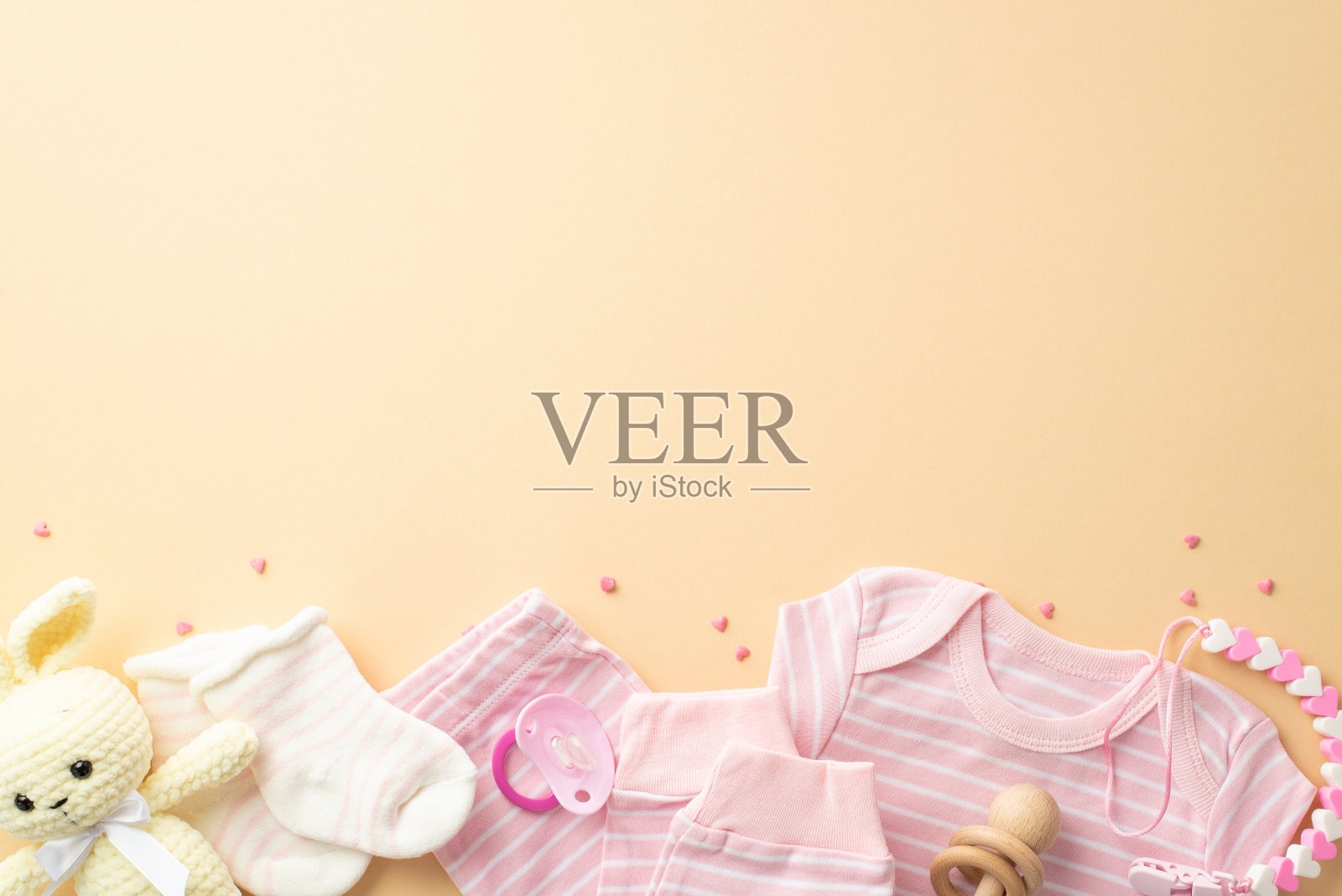 女婴概念。婴儿衣服粉红色衬衫裤子袜子针织兔子玩具木制拨浪鼓安抚奶嘴牙链和洒水孤立粉彩黄色背景与复制空间照片摄影图片