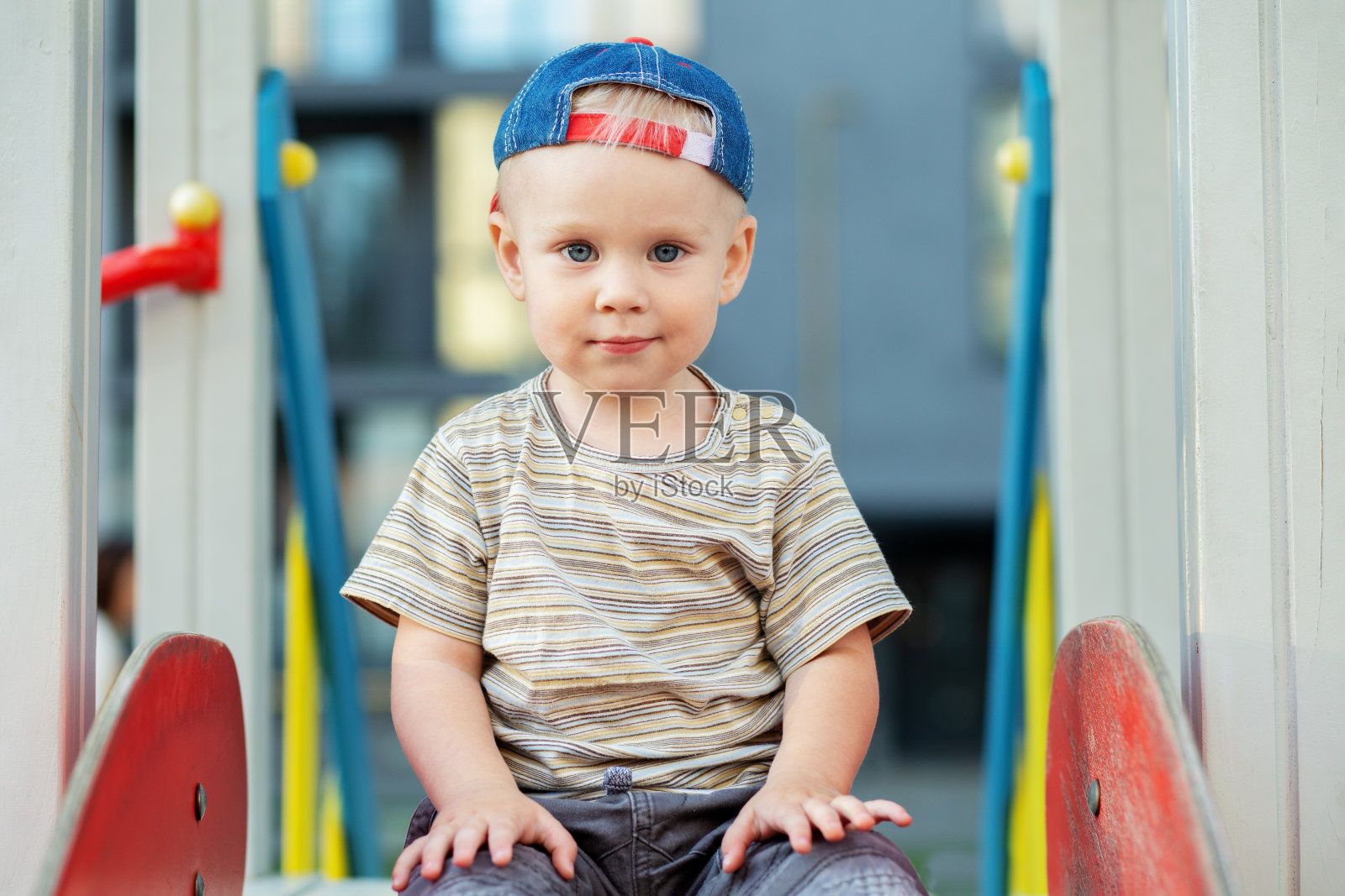 可爱的两岁男孩玩游乐场滑梯在夏天。孩子们在幼儿园的院子里玩耍。照片摄影图片