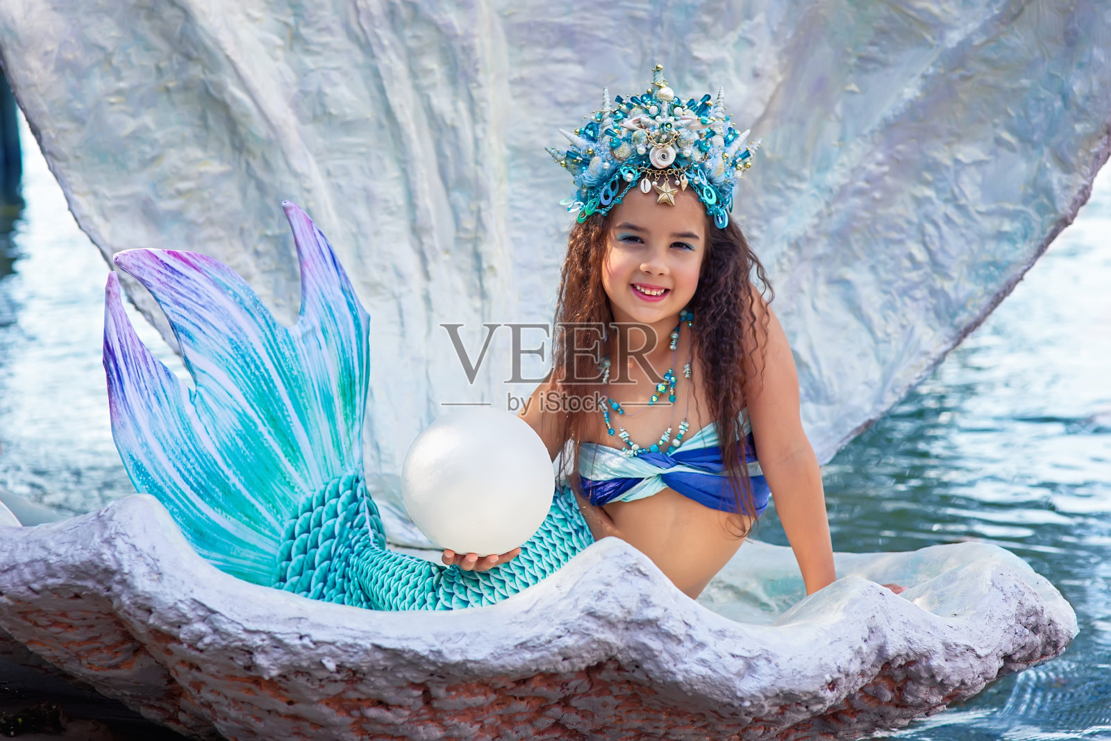 一个美丽快乐的小女孩穿着美人鱼服装坐在一个大贝壳里照片摄影图片