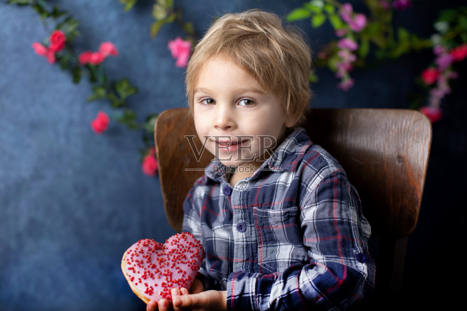 可爱的金发小孩，学龄前男孩，吃着心形的粉色甜甜圈，情人节礼物照片摄影图片