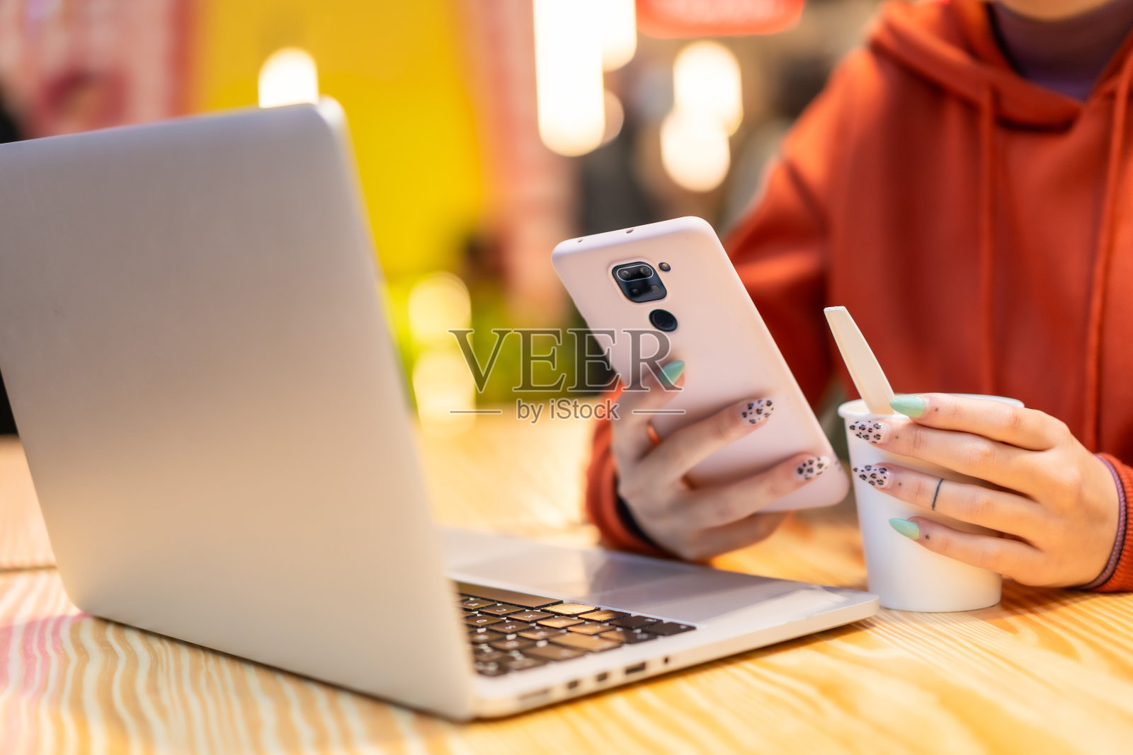 女士的手用她的手机端着咖啡坐在桌子上的笔记本电脑前照片摄影图片