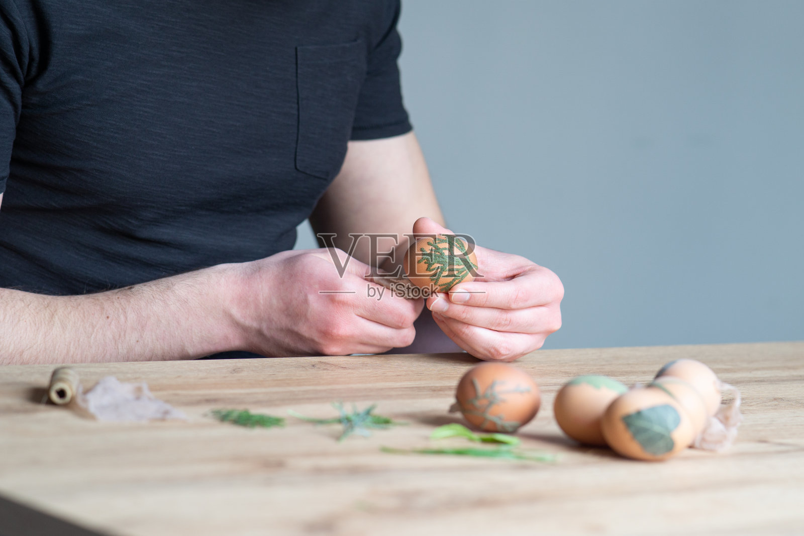 男性的手用不同类型的叶子装饰复活节彩蛋的特写。用树叶装饰复活节彩蛋的有趣方法。用叶子装饰鸡蛋。年轻人在装饰复活节彩蛋。照片摄影图片