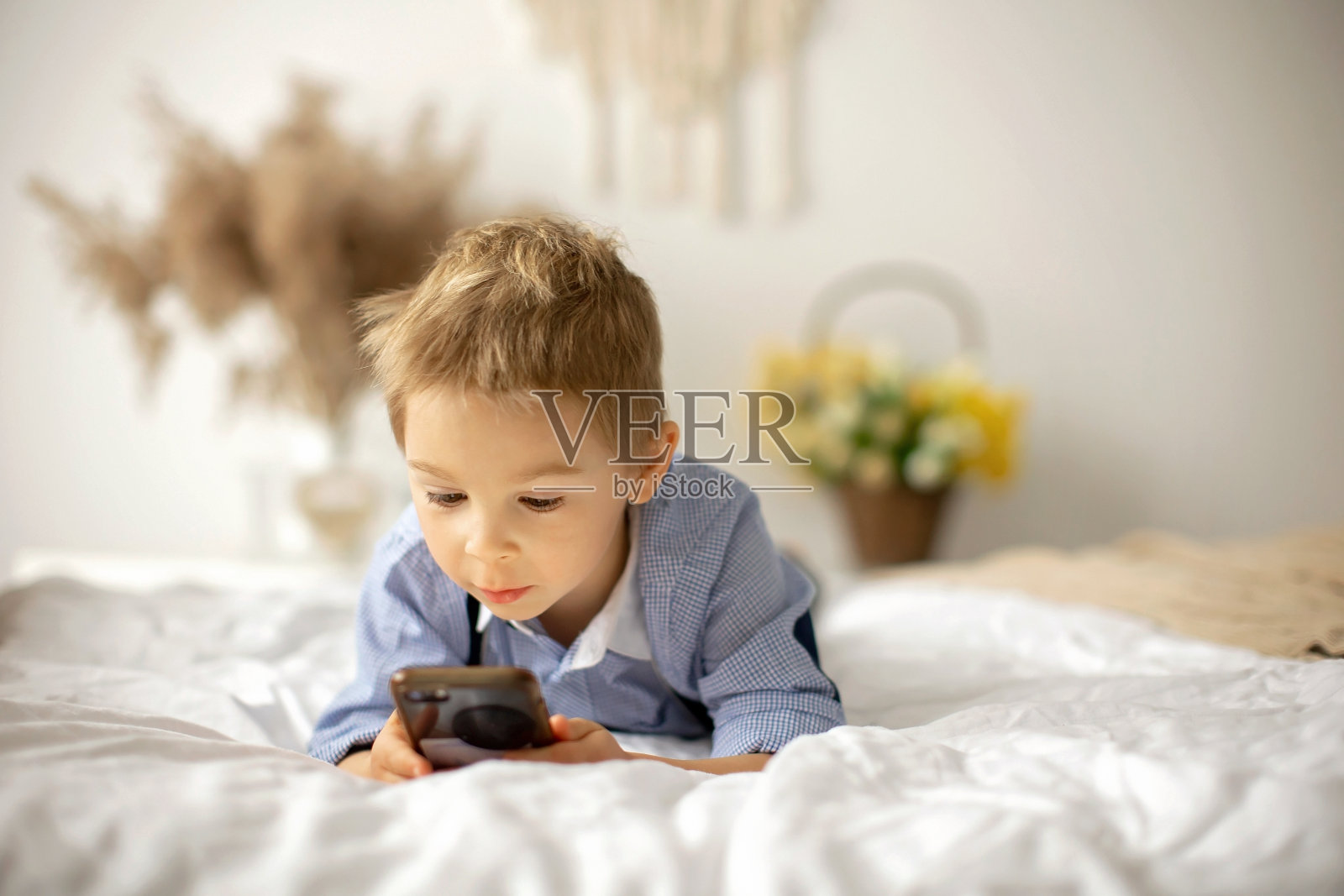 金发学龄前儿童，可爱的男孩，在床上玩手机照片摄影图片