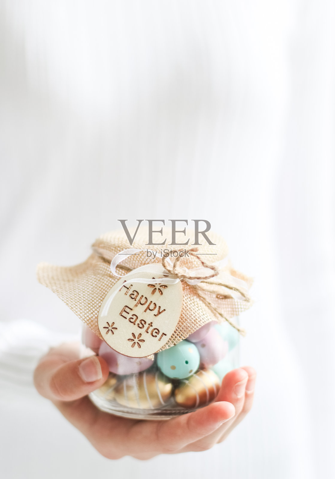 一位高加索少女穿着白色高领毛衣，手里拿着一个装有彩色鸡蛋的可爱玻璃罐照片摄影图片