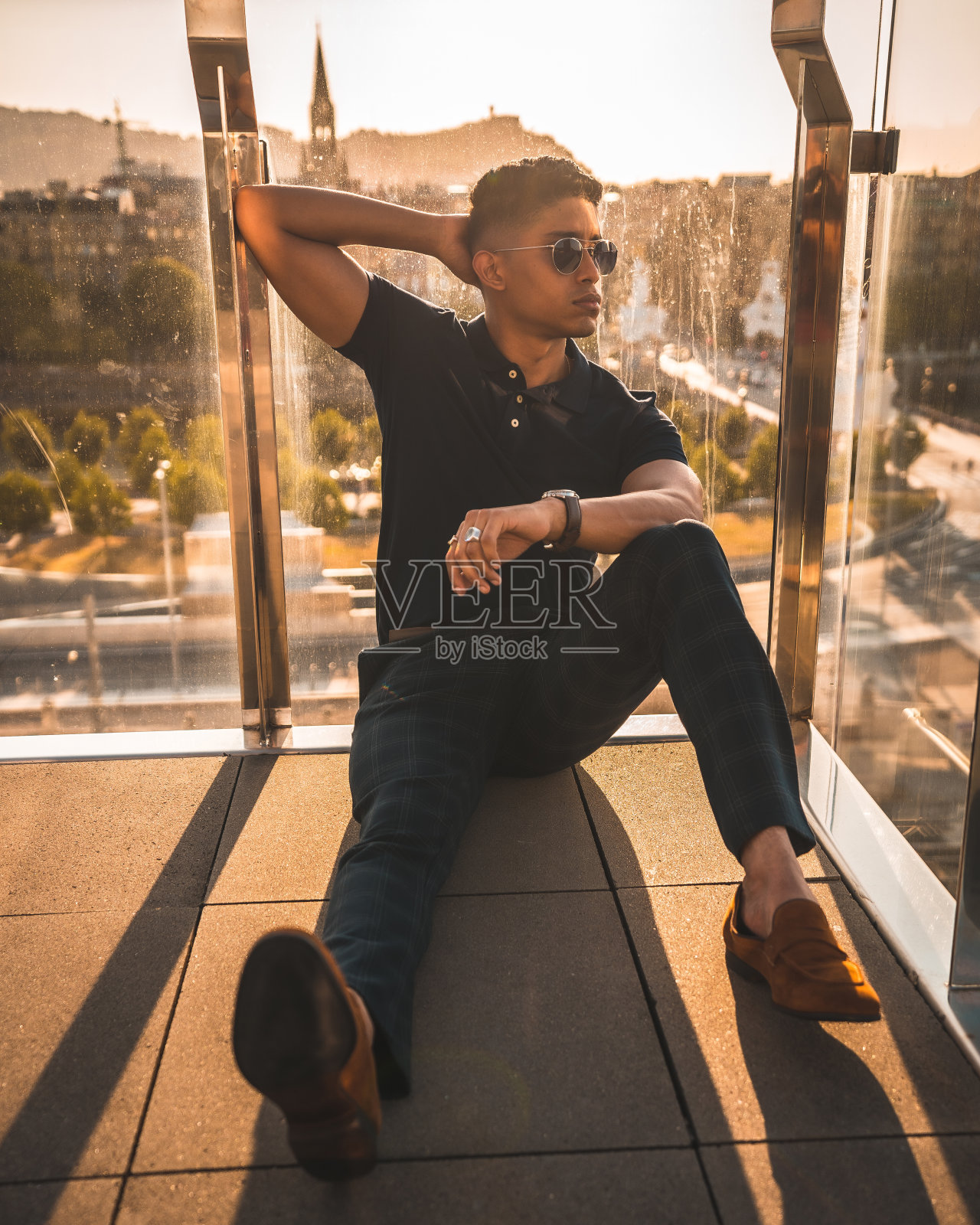 帅气的西班牙人戴着墨镜坐在阳台地板上摆姿势照片摄影图片