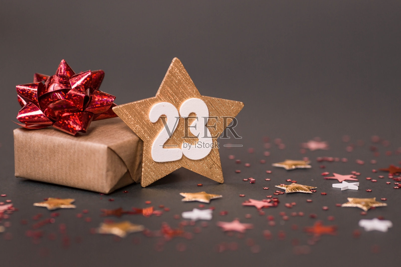 给祖国保卫者节的贺卡。白色，金色，红色星星，一个礼品盒，棕色背景上的数字23。假期是2月23日。照片摄影图片