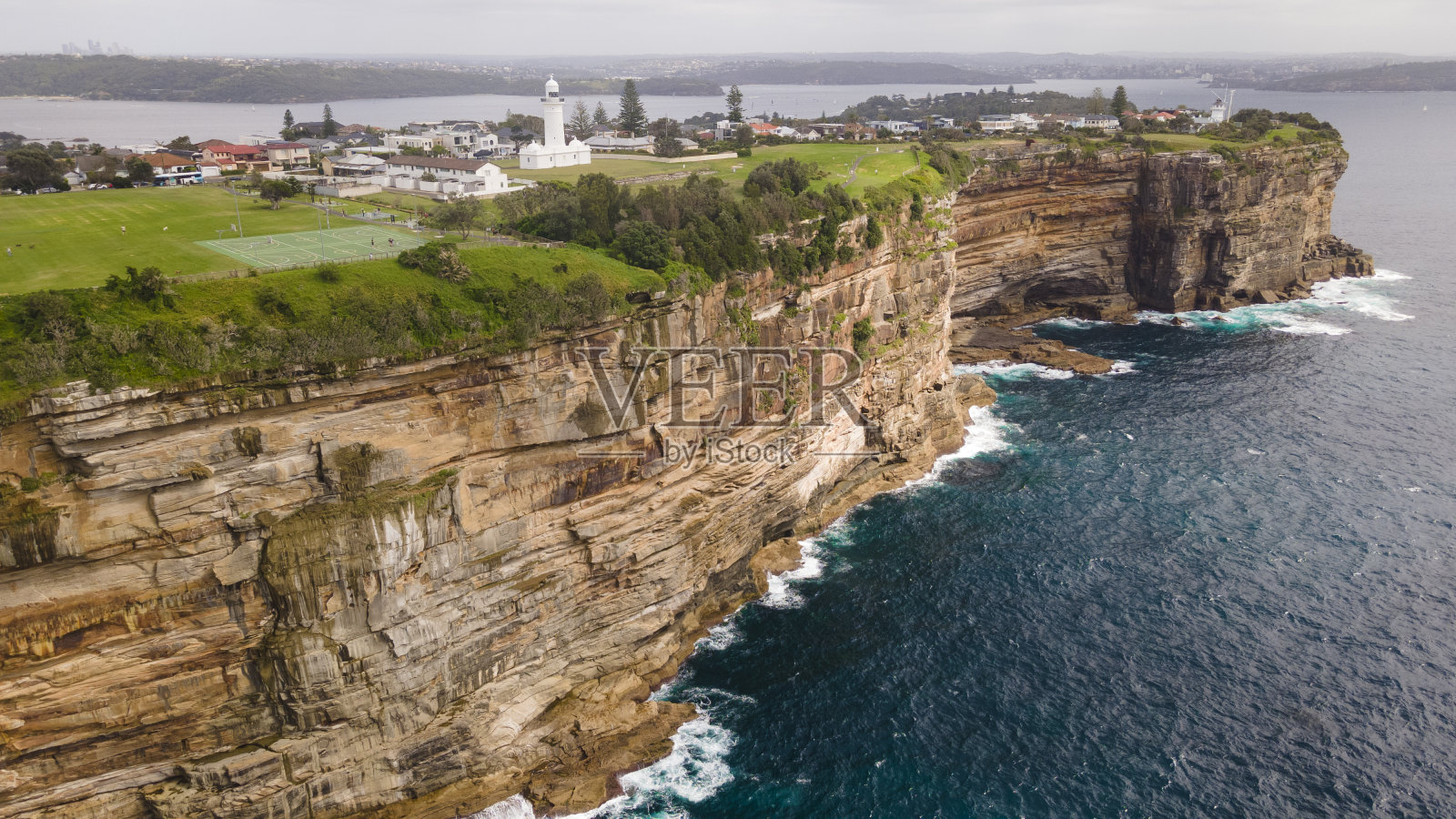 在新南威尔士州东悉尼的沃克卢兹，沿着风景优美的海岸悬崖顶部俯瞰邓巴岬的麦考瑞灯塔的无人机鸟瞰图照片摄影图片