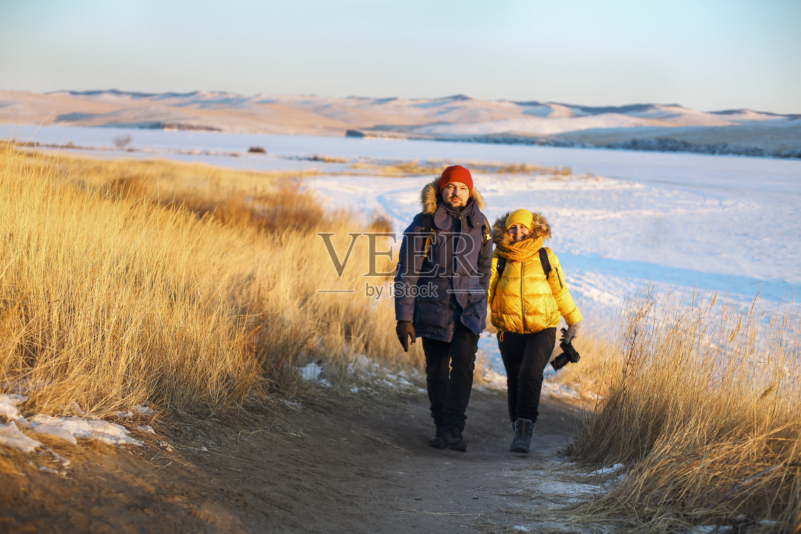 一对浪漫的游客情侣穿着温暖的冬季运动服，背着旅游背包走在雪地里照片摄影图片