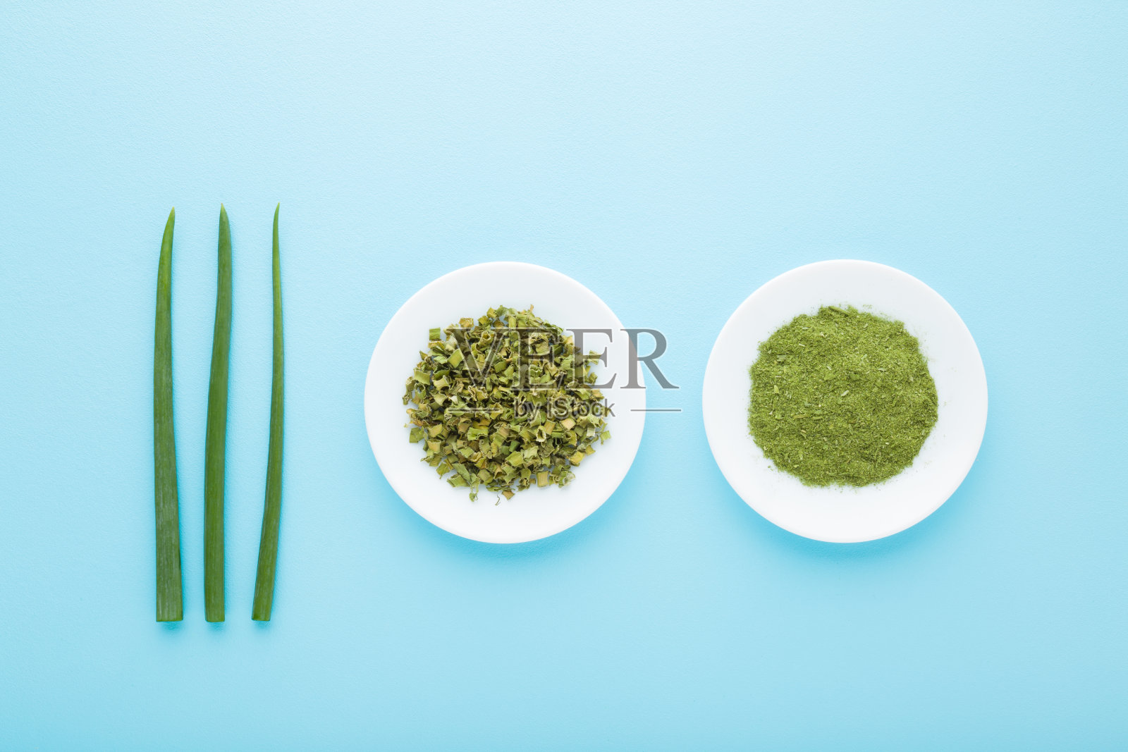 新鲜的大葱，干切和洋葱粉放在浅蓝色桌子背景的白色盘子上。柔和的颜色。香料的制备和储存方式不同。特写镜头。自顶向下视图。照片摄影图片