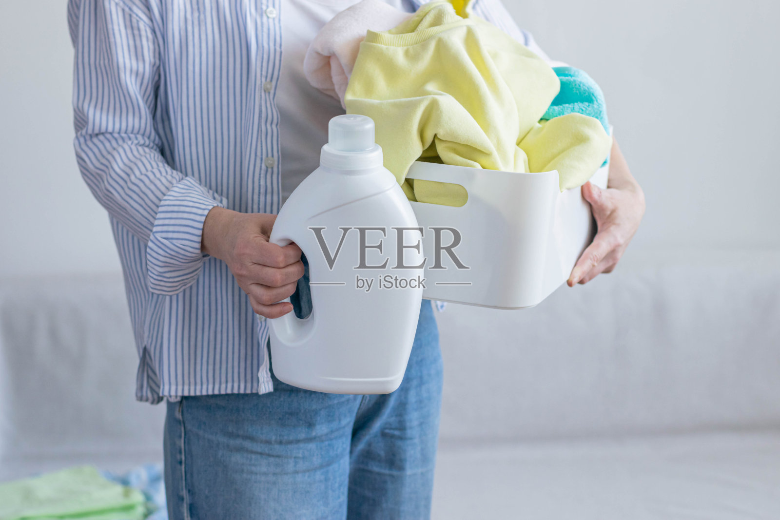 女人手里拿着装满脏衣服的洗衣液的篮子。粉状凝胶助剂织物柔顺剂。照片摄影图片