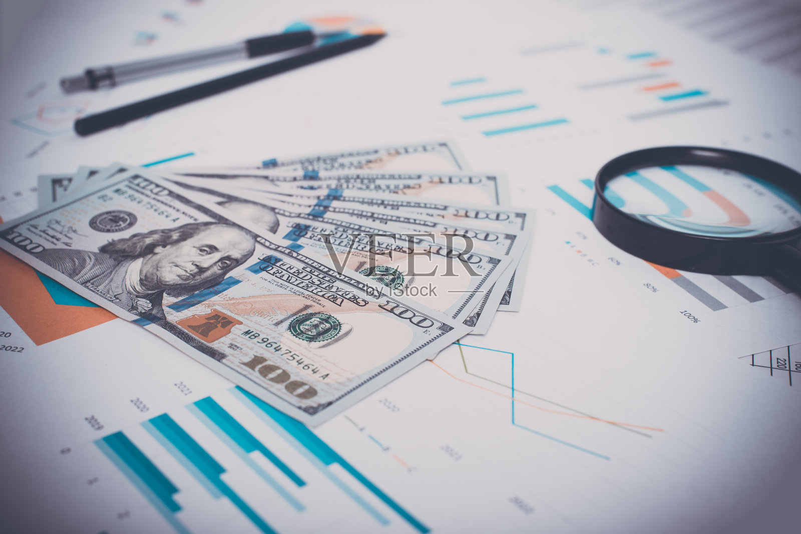 工作场所的金钱、商业文件、放大镜、钢笔和铅笔特写。低角度视角，选择性聚焦于百元大钞照片摄影图片