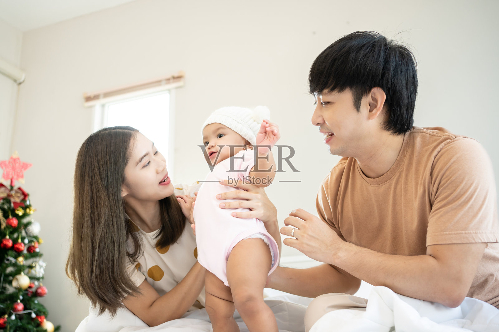 微笑的父母抱着他们刚出生的女儿在家里。卧室里的亚洲家庭肖像。照片摄影图片