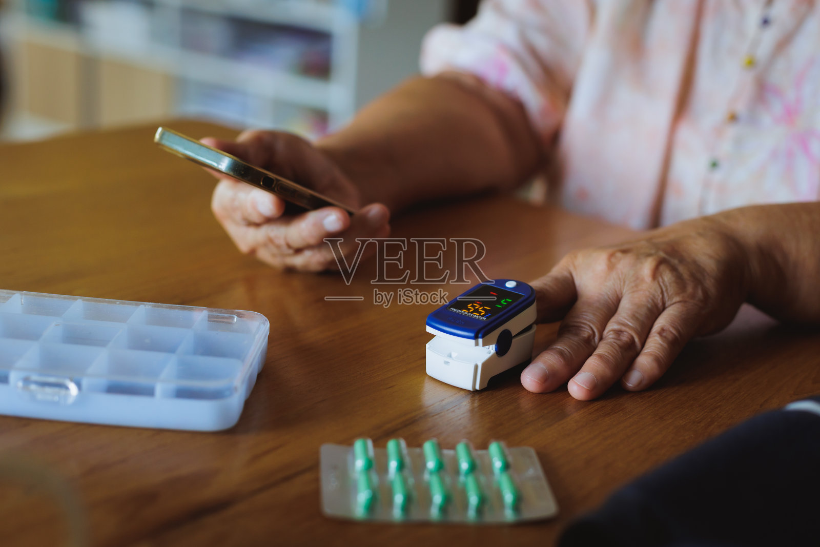 一名年长的亚洲妇女在家用手指上的脉搏血氧计自测血氧水平，并将结果记录在智能手机上。照片摄影图片