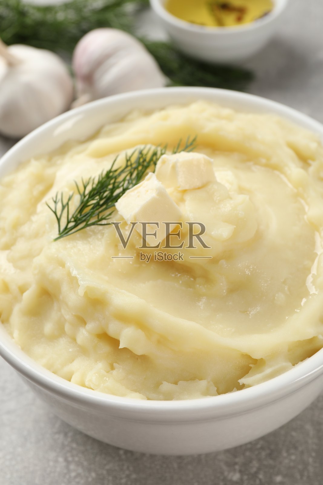 一碗美味的土豆泥配上莳萝和黄油放在浅灰色的桌子上，特写照片摄影图片