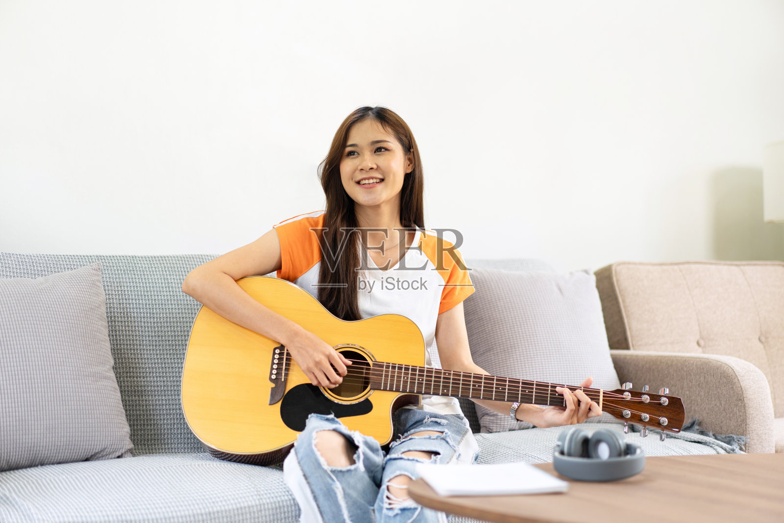 年轻女子正在弹吉他，练习唱歌，坐在舒适的沙发上照片摄影图片