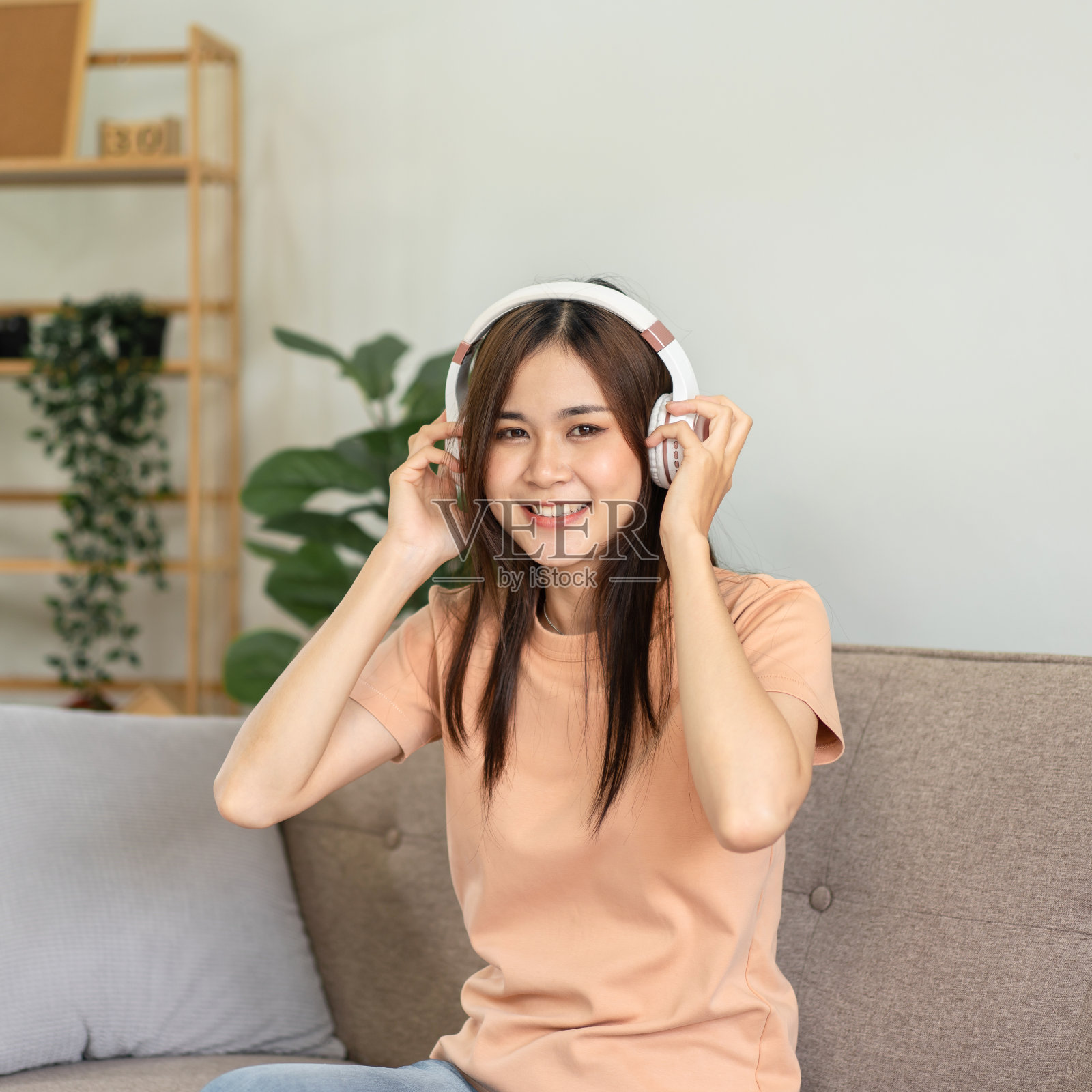 年轻的亚洲女子是触摸耳机与双手听音乐和唱歌，而坐着照片摄影图片