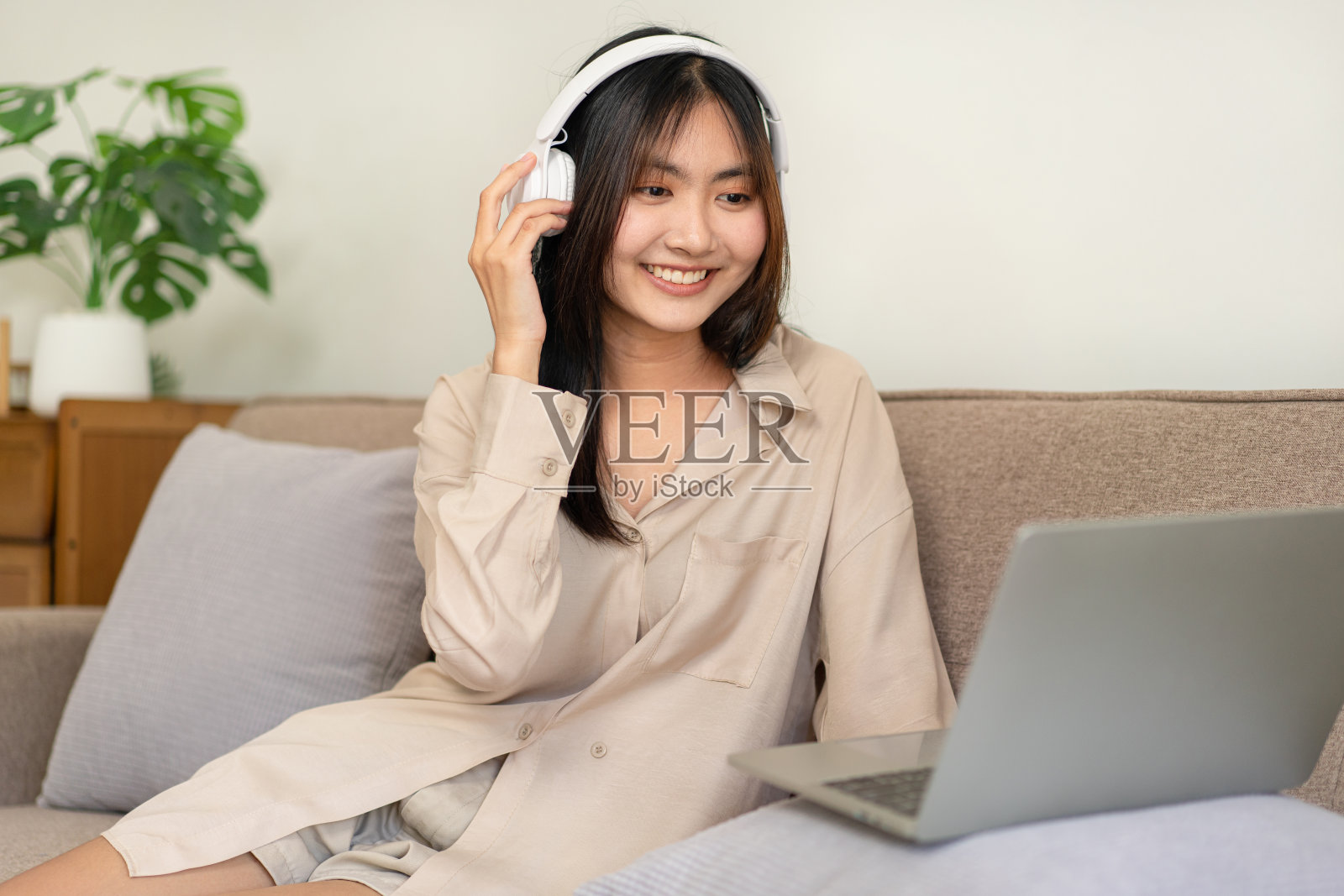 女企业家坐在舒适的大沙发上，把笔记本电脑放在枕头上，摸着耳机照片摄影图片