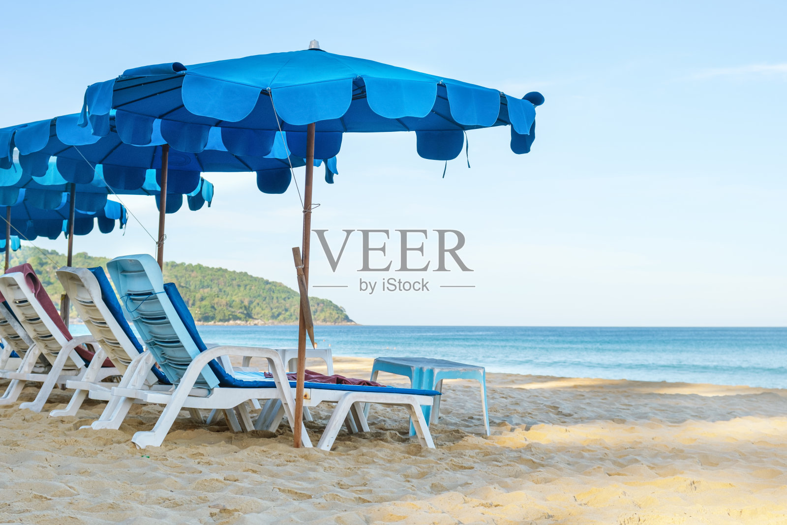 沙滩上的沙滩椅和蓝色雨伞，以大海为背景照片摄影图片