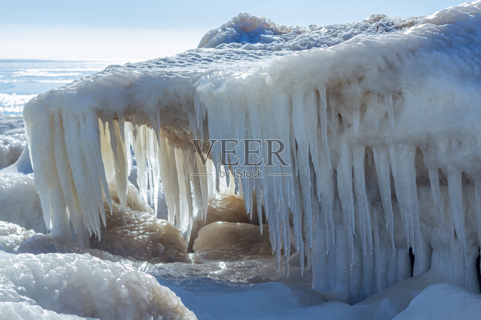 特写的冰冷的海岸，冻结的波浪，岩石和太阳在冰上眩光照片摄影图片