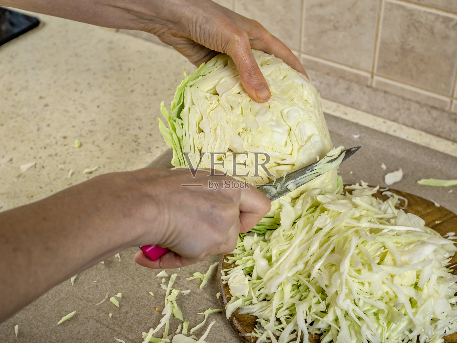 家庭主妇的手在厨房桌子上的木制砧板上切白卷心菜。在家里的厨房里做生蔬菜。新鲜蔬菜有益于健康和长寿照片摄影图片