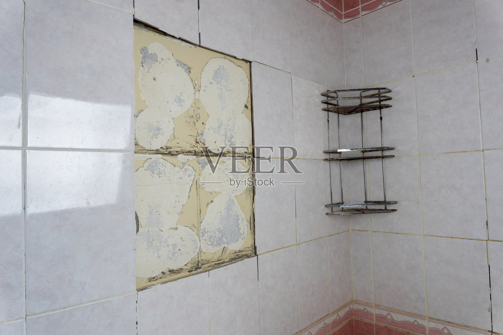 破旧的浴室，瓦片掉落。一个旧架子。一面剥落的墙照片摄影图片