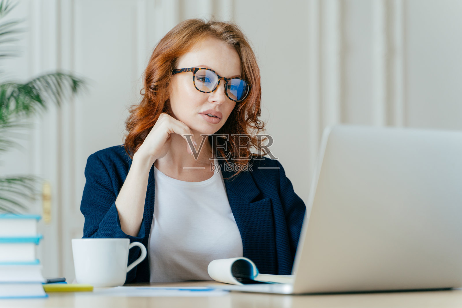 迷人的女商人镜头集中在笔记本电脑显示器上，目光严重集中，戴视力矫正眼镜，看训练视频，喝热饮照片摄影图片