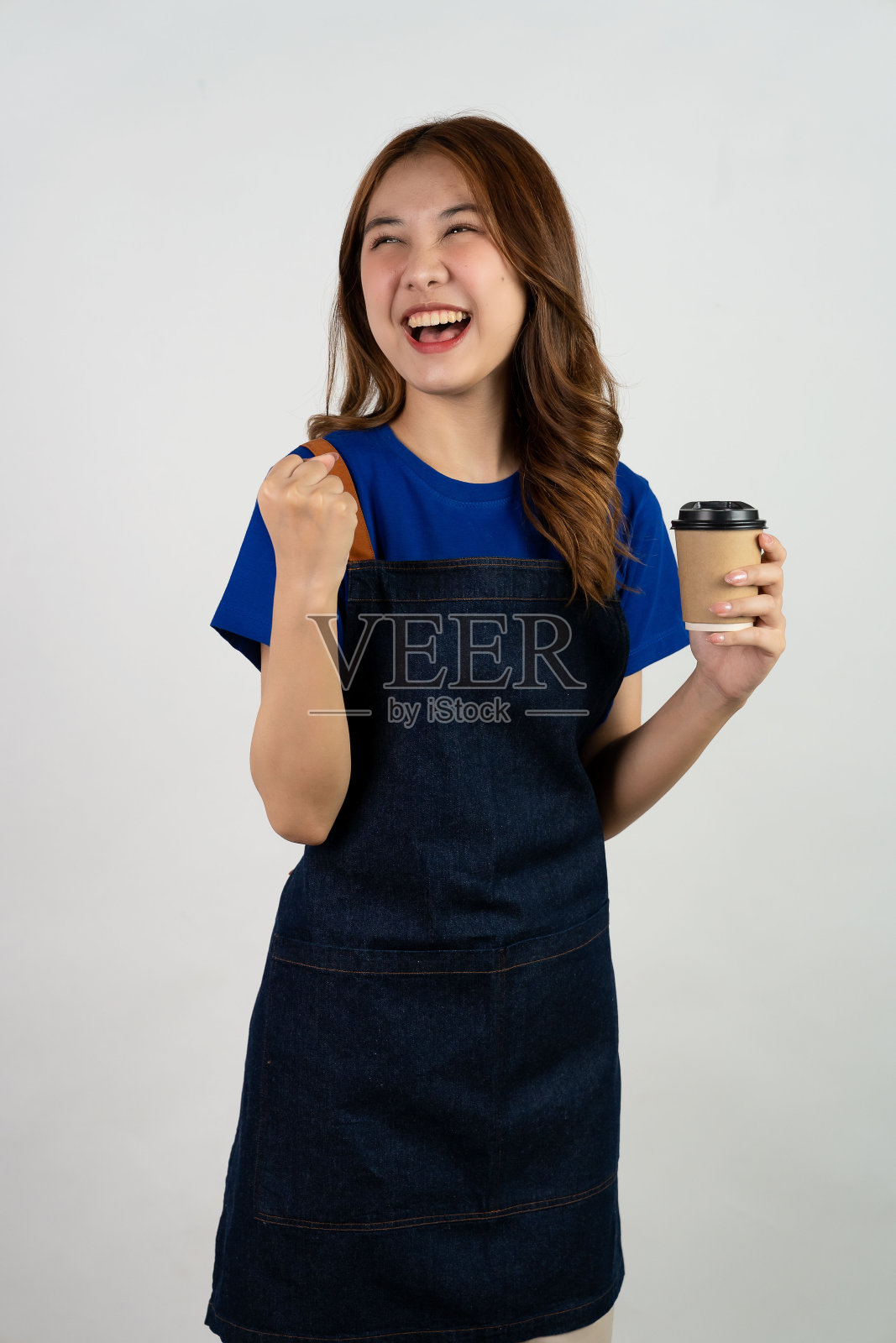 迷人的年轻女子拿着一杯咖啡师咖啡饮料，亚裔女调酒师在围裙拿着纸咖啡杯出售热饮茶孤立在白色背景照片摄影图片