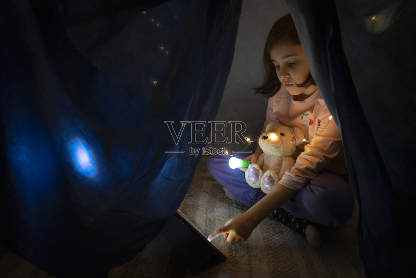 小女孩晚上在卧室的帐篷里用平板电脑看书照片摄影图片