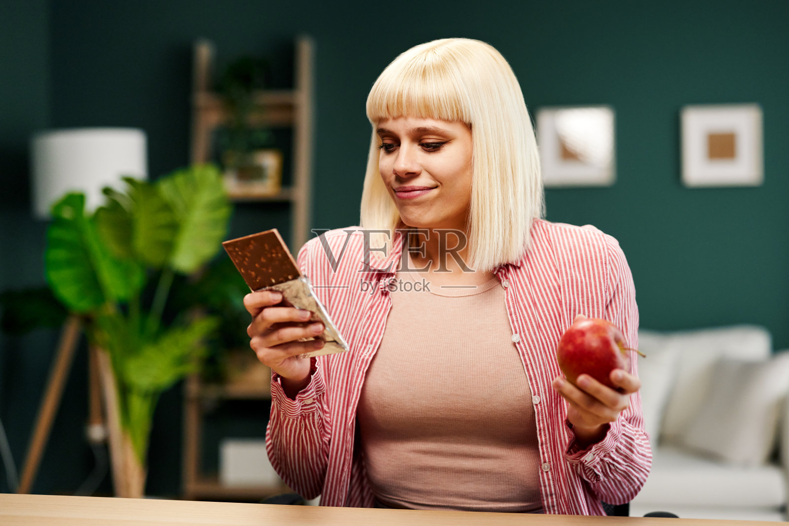 年轻的金发女子手里拿着一块巧克力和一个苹果，不知道该吃什么照片摄影图片