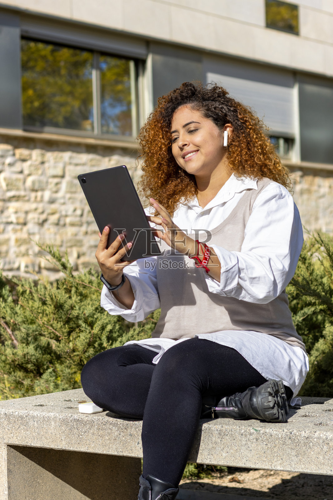 穿着西装的女孩坐在学校的河岸上，拿着平板电脑在线听音乐照片摄影图片
