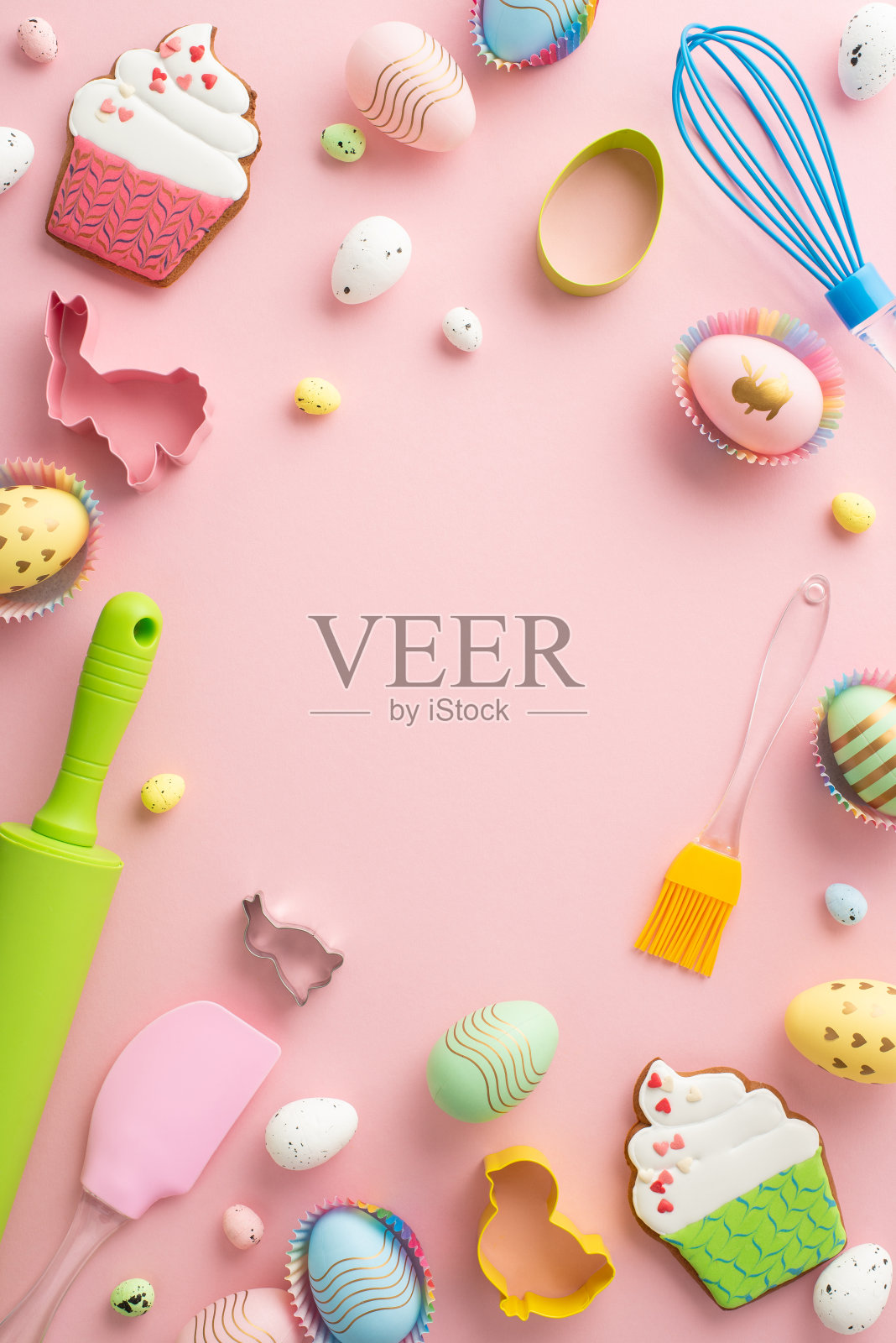俯视图垂直照片的擀面棍搅拌硅胶锅铲彩色复活节彩蛋在纸烘焙模具和蛋糕形状的姜饼在孤立的粉彩粉红色背景与中间的空白照片摄影图片