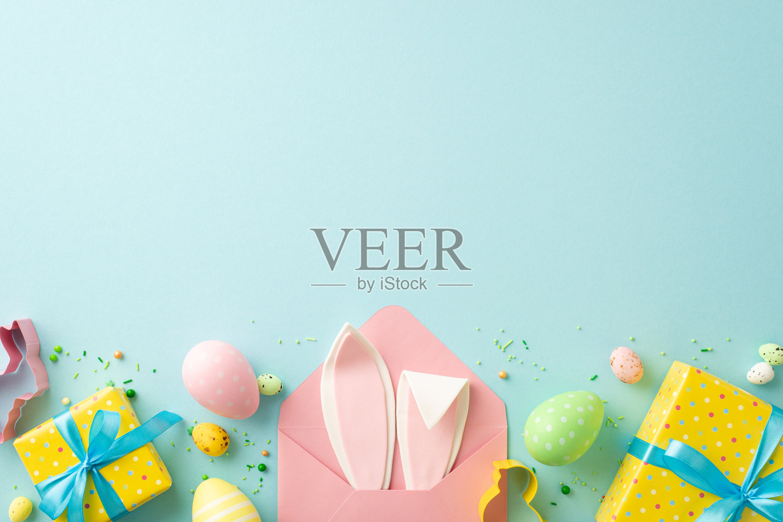 复活节的概念。顶部视图照片打开粉红色信封兔耳朵黄色礼品盒与蓝色蝴蝶结彩色复活节鸡蛋烘焙模具洒在孤立的粉彩蓝色背景与复制空间照片摄影图片
