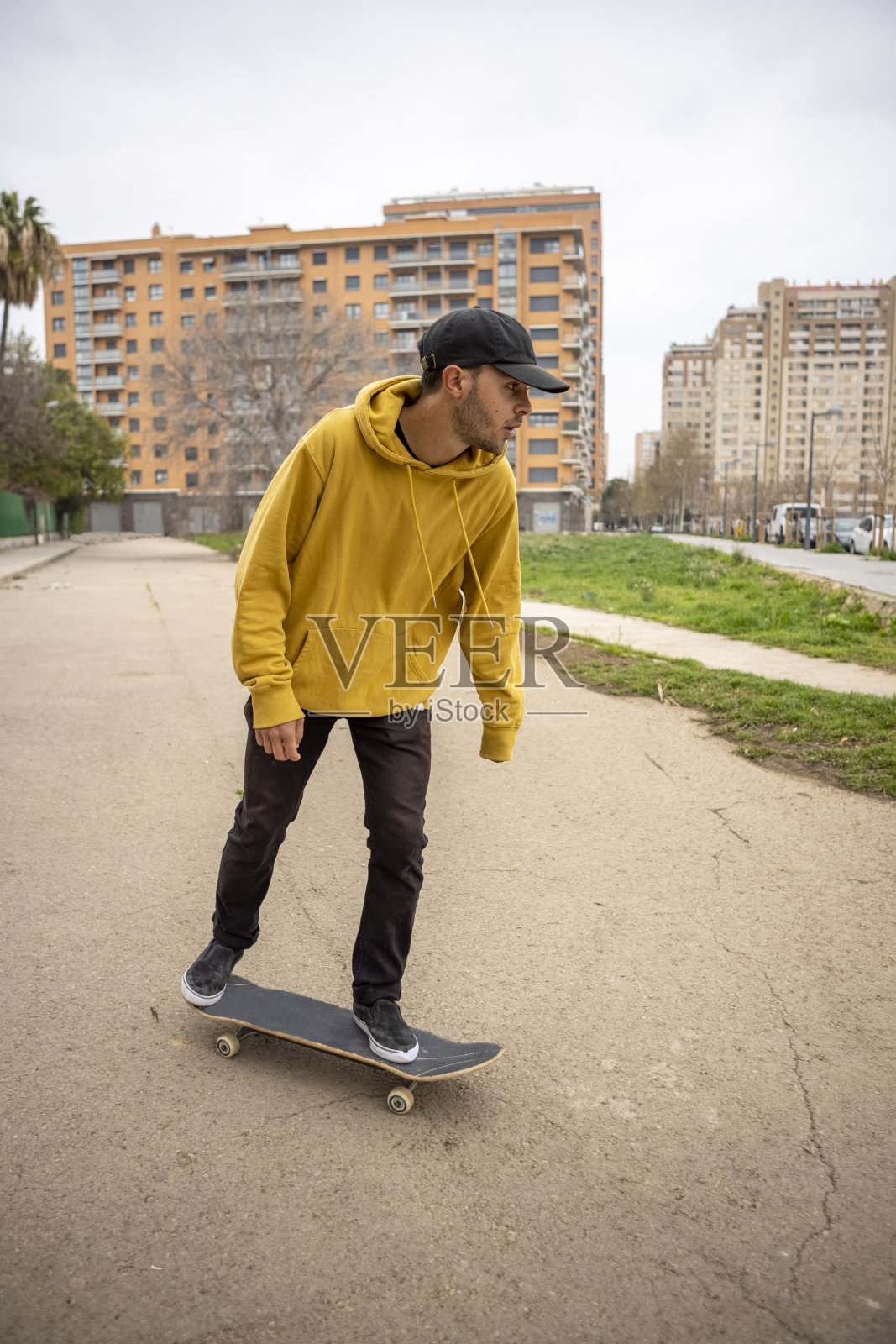 来自意大利的年轻白人男子，穿着黄色卫衣，戴着黑色帽子，站在滑板上照片摄影图片
