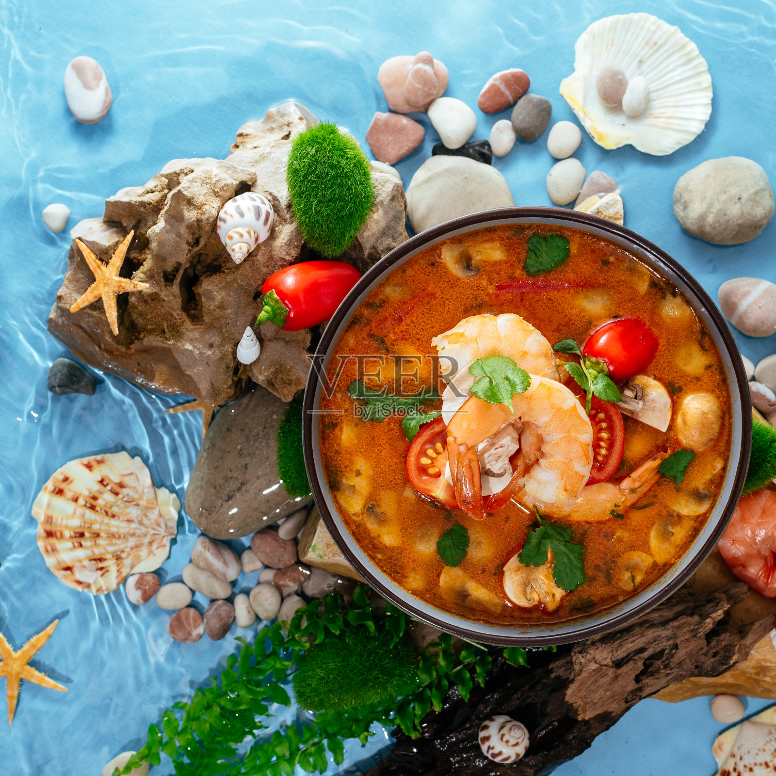 亚洲冬阴虾汤。盘子在水里的岩石上照片摄影图片