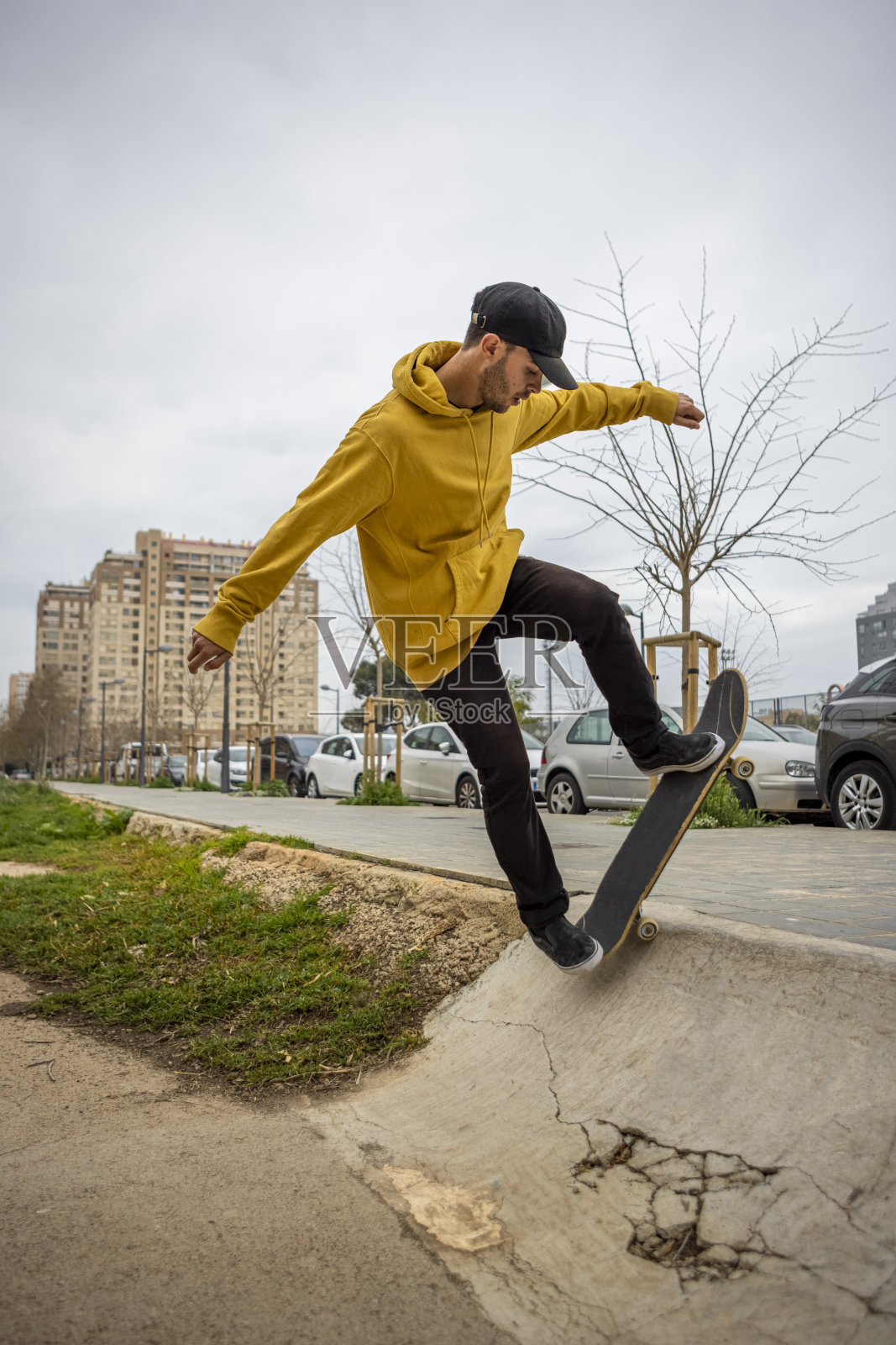 来自意大利的年轻白人男子，穿着黄色连帽衫，戴着黑色帽子，玩着滑板照片摄影图片