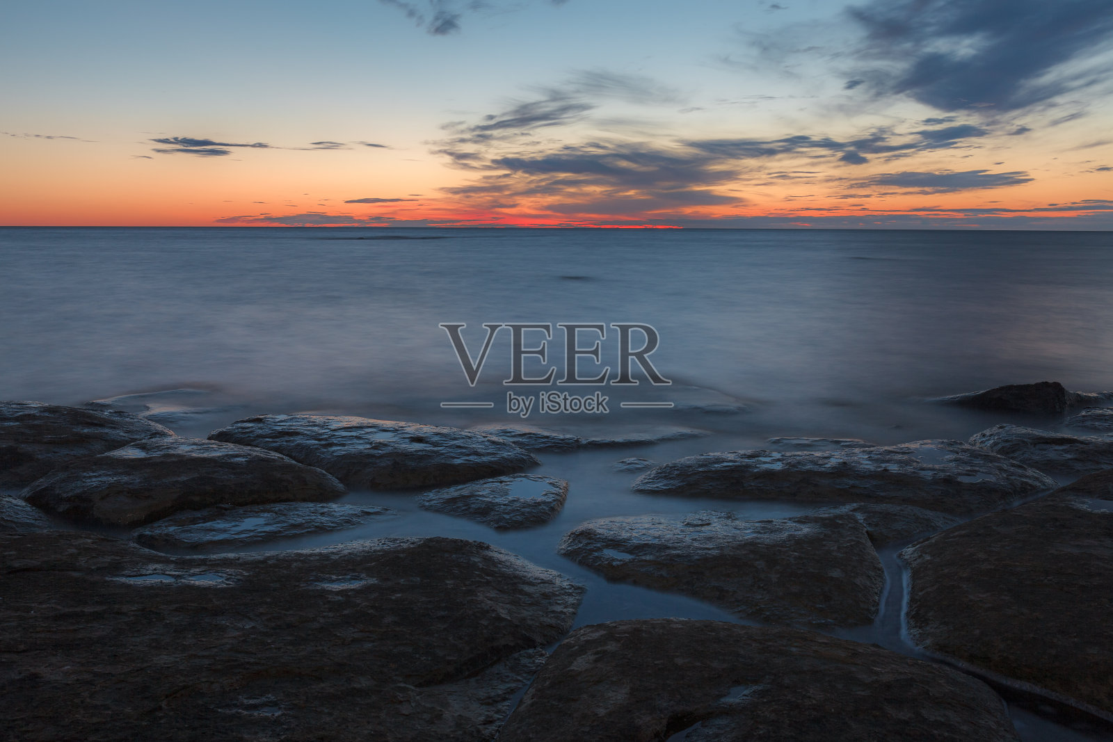 波罗的海岩石海岸的黄昏日落。几乎晴朗的天空和橙色的带子沿horison。爱沙尼亚。照片摄影图片